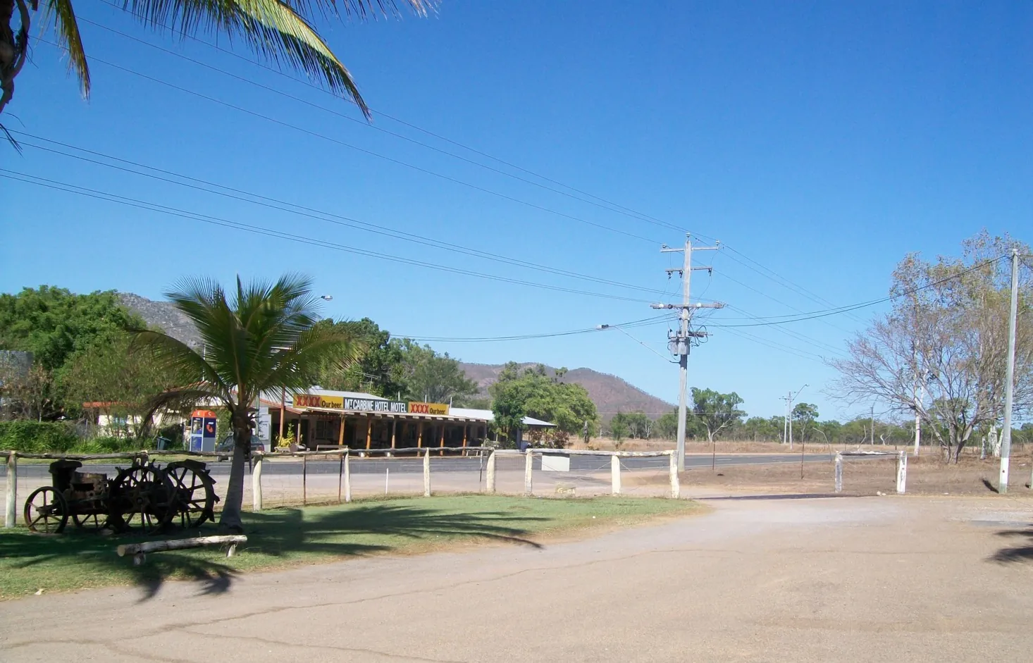 A roadside township with a pub and old machinery under a blue sky